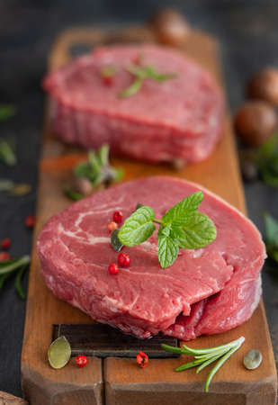 Raw beef fillet steaks on wooden board on dark background close up. Portioned filet mignons with spices and herbs. Concept of summer foodの写真素材