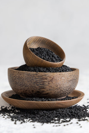 Indian spice Black cumin (nigella sativa or kalonji) seeds in wooden bowls on white table close up. Traditional medicine, healthy and vegetarian food concept.の写真素材