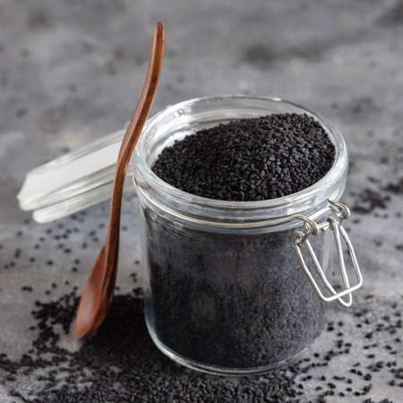 Indian spice Black cumin (nigella sativa or kalonji) seeds glass jar with a wooden spoon, close up. Traditional asian medicine, healthy and vegetarian food conceptの写真素材