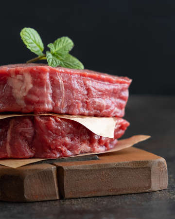 Raw beef fillet steaks on wooden board on dark background close up. Portioned filet mignons with spices and ingredients. Concept of summer foodの写真素材