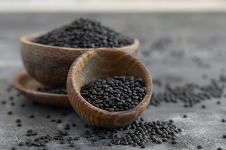Wooden bowls of black beluga lentils beans on grey table close up.  Healthy eating, protein source...