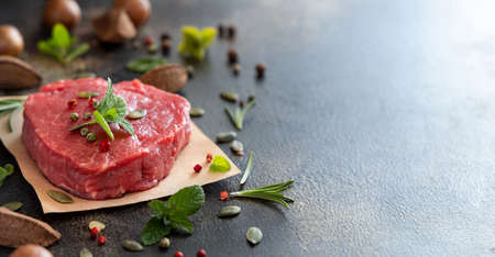 Raw beef fillet steaks on dark table close up with copy space. Portioned filet mignon with spices and herbs. Concept of summer food, meat eaters.の写真素材