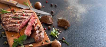 Grilled beef fillet steaks on dark table close up. Portioned filet mignon with spices and herbs. Concept of summer food, meat eaters.の写真素材