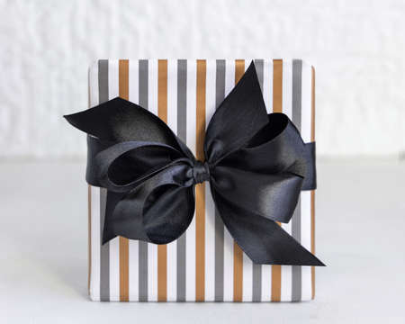 Gift box wrapped in Striped geometric paper with black ribbon bow close up. Christmas, New Year, Birthday, Anniversary conceptの写真素材