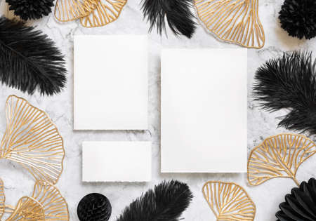 Blank cards on marble table near black feathers and golden leaves top view. Wedding set mockup. Elegant femminine suite with paper cards, flat layの写真素材