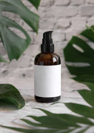 Brown one pump dispenser and tropical monstera leaves on marble table close up. Brand packaging mockup. Skincare beauty product. Natural herbal cosmetics conceptの写真素材