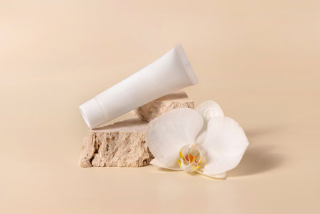 White cream tube on travertine stone near white orchid flower on light yellow, close up, mockup. Skincare handmade beauty product, cream or lotion. Exotic natural cosmeticsの写真素材
