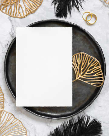 Black and golden wedding table setting with a blank card top view, mockup. Elegant flat lay with vertical greeting or Invitation paper card, wedding or holiday stationery templateの写真素材