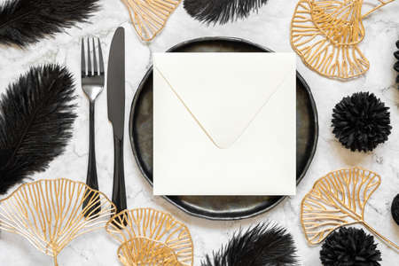 Black and golden wedding table setting with a blank square envelope top view, mockup. Elegant modern holiday flat lay, wedding or holiday stationery templateの写真素材