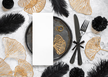 Black and golden wedding table setting with a blank card and rings top view, mockup. Elegant flat lay with vertical menu or Invitation paper card, wedding or holiday stationery templateの写真素材