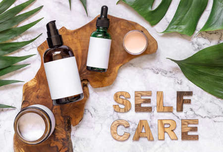 Self Care text near cosmetic bottles and monstera leaves, copy space. Brand package mockup. Natural beauty products, Top viewの写真素材