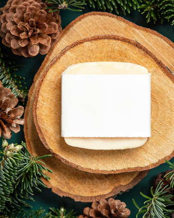 Natural soap bar between fir branches and pine cones on wooden piece top view. Brand package mockup. Health care concept. Handmade cosmetics. Winter conceptの写真素材