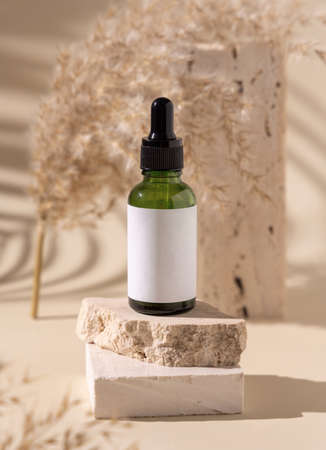 Green dropper bottle on travertine stone near dry pampas grass on light yellow, close up, mockup. Skincare beauty product. Natural cosmetics. Boho compositionの写真素材