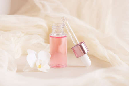 Light Pink opened Dropper Bottle near white orchid flower on light yellow, close up, mockup. Skincare beauty product, Aromatic oil or serum. Exotic cosmetics, pastel minimal compositionの写真素材