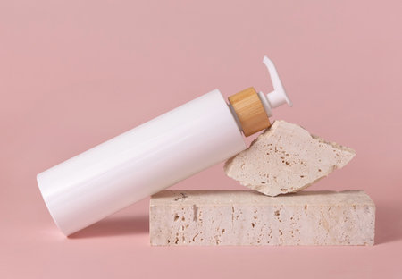 White one pump bottle lies on travertine stone on light pink, close up, mockup. Skincare beauty product. Natural cosmetics, lotion or cleanser. Minimal compositionの写真素材