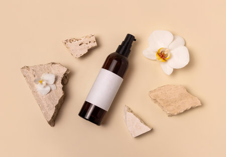 Dark glass cosmetic bottle near white orchid flowers and stones on light yellow, top view, mockup. Skincare handmade beauty product, tonic or lotion. Exotic natural cosmeticsの写真素材