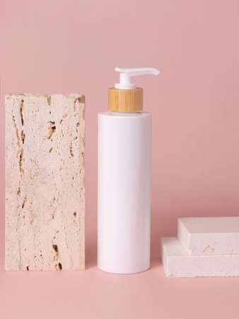 White one pump bottle near beige travertine stone on light pink, close up, mockup. Skincare beauty product. Natural cosmetics, lotion or cleanser. Minimal compositionの写真素材