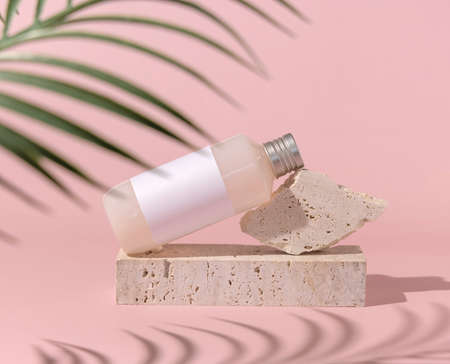 Cosmetic bottle with blank label lies on stone on light pink, palm leaf hard shadow , close up, mockup. Skincare beauty product. Natural cosmetics, lotion or cleanserの写真素材