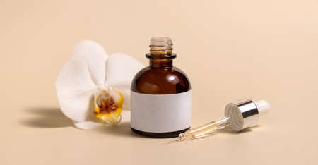 Brown glass dropper bottle near white orchid flowers on light yellow, close up, mockup. Skincare handmade beauty product, serum or lotion. Exotic natural cosmeticsの写真素材