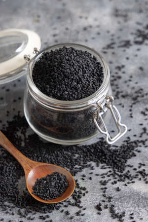 Indian spice Black cumin (nigella sativa or kalonji) seeds glass jar with a wooden spoon, close up. Traditional asian medicine, healthy and vegetarian food conceptの写真素材