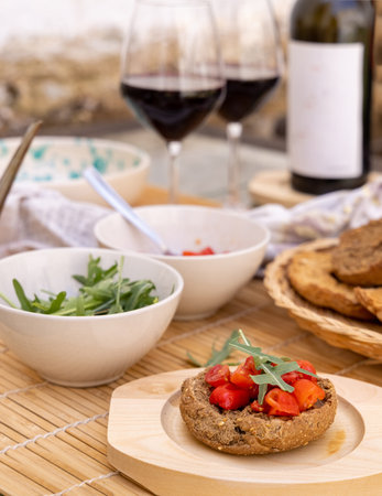 Italian summer appetizer Friselle with cherry tomatoes, oil and rucola served outdoor with glasses of red wine. Tipical Apulian Dried bread, made in Salento. Local cousine. Vegetarian foodの写真素材