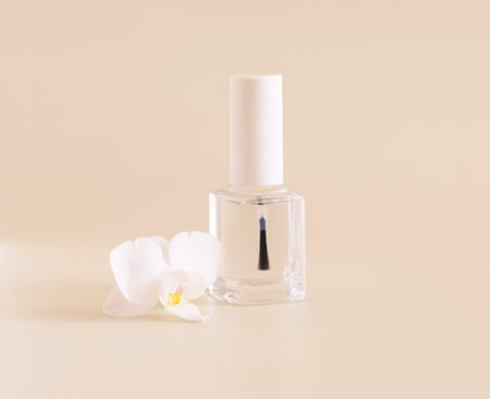 Clear Glass Refillable Bottle with Brush Cap near white orchid flower on light yellow, close up, mockup. Skincare nail product. Exotic natural cosmetics, pastel minimal compositionの写真素材