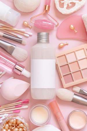 Bottle with blanik label, skin care and decorative cosmetics on pink, top view, mockup. Flat lay with natural beauty products and decorative cosmetics. Everyday woman face care routineの写真素材