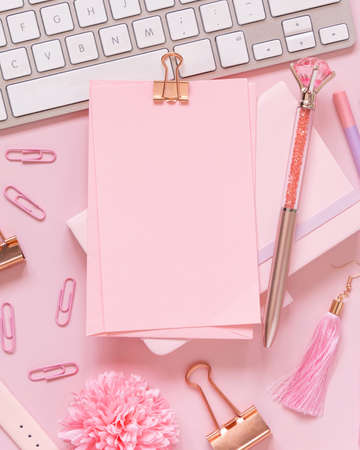 Paper with a clip, pink accessories and keyboard on pastel pink, top view, mockup. Girly workplace. Back to school conceptの写真素材