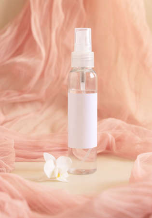 One pump dispenser bottle near white orchid flowers againts light pink tulle close up, mockup. Skincare beauty product package. Exotic natural cosmetics, pastel minimal compositionの写真素材