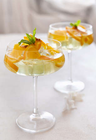 Transparent cocktail with ice cubes in a champagne coupe glass decorated with slices of orange close up. Tropical drink at the bar. Summer vacation moodの写真素材