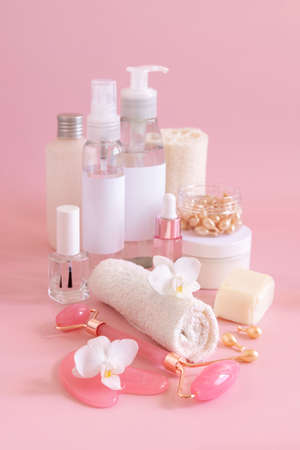 Natural cosmetic jars, skin care accesories and rose quartz face massagers with white orchid flower on light pink close up. Beauty products mockup. Everyday woman face care routine, Spa Treatmentsの写真素材