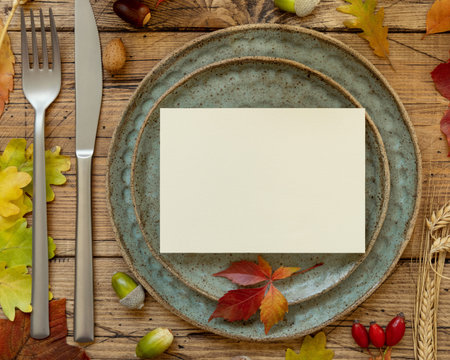 Autumn rustic table setting with blank card between colorful leaves and berries, top view....