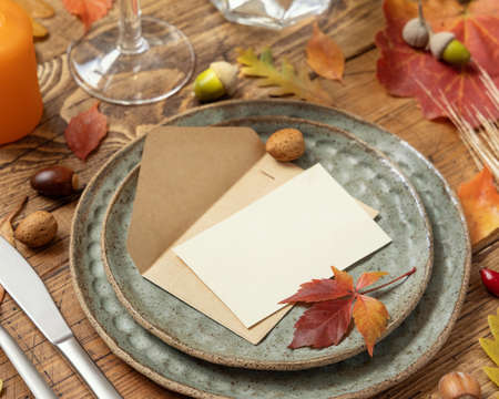 Autumn rustic table setting with blank place card and envelope between colorful leaves and berries close up, mockup. Flat lay Horizontal card on wooden table, flat lay, copy space. Thanksgiving or harvestの写真素材