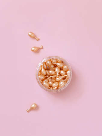 Beauty serum capsules in a jar on light pink top view. Skincare beauty product. Facial cosmetics, pastel minimal compositionの写真素材