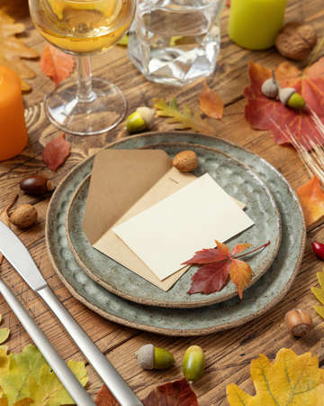 Autumn rustic table setting with blank place card and envelope between colorful leaves and berries, close up, mockup. Flat lay Horizontal card on wooden table, flat lay, copy space. Thanksgiving or harvestの写真素材