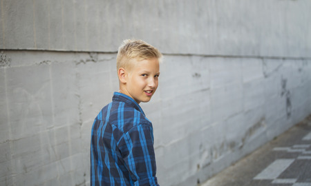 Boy's portrait in a blue shirt against a gray concrete wallの写真素材