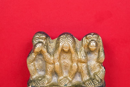 Souvenir figurines of the three monkeys, symbolizing the Buddhist idea of non-doing of evil, detachment from false. See nothing, hear nothing, say nothing. Isolated on red background.の写真素材