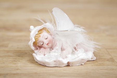 Miniature statue of a white little cute angel with featgers wings on wooden surface.の写真素材