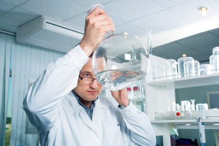 Laboratory assistant in white coat looking in a bottles with pure liquid.