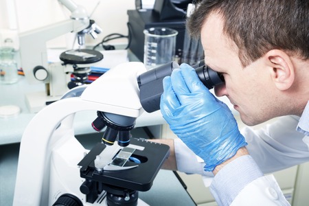 Portrait of caucasian male chemist scientific researcher using microscope in the laboratoryの写真素材