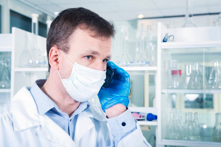 Portrait of caucasian male chemist scientific researcher in blue rubber gloves and white coat using...