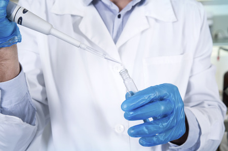 Caucasian male chemist scientific researcher in medical mask, blue rubber gloves and white coat using test tubescultivating whit inoculation loops in pipette at his workplace in the laboratory.の写真素材