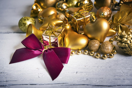 Brilliant gold baubles and cones like christmas decoration. Yellow balls ribbon, gift, red bow and tinsel isolated on white wooden background.の写真素材