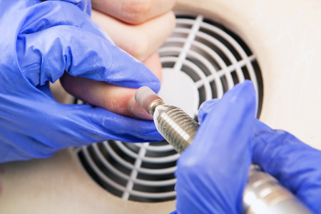 Manicure specialist care by finger nail in beauty salon. Electric nail file. Gel nails.  Manicurist uses professional manicure tool.  の写真素材