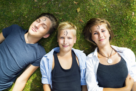Smiling boys and girl (siblings) are lying on green grass in nature sunny day. Concept of positive thoughts and emotions.の写真素材