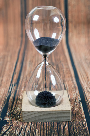 Hourglass, iron sand measuring the passing time in a countdown to a deadline,on wooden backgroundの写真素材