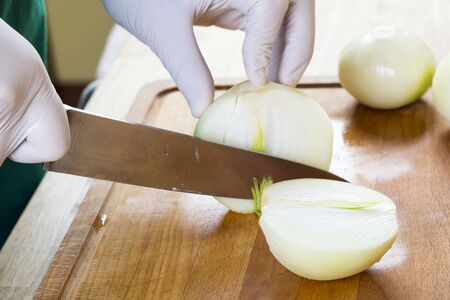 Chef's hands with knife cutting the onion on the wooden board. Preparation for cooking. Healthy eating and lifestyle.の写真素材