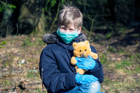 Child in protective sterile medical mask on his face looking at camera outdoors. Air pollution,...