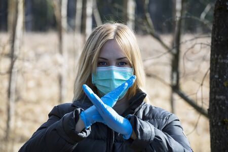 Woman in protective sterile medical mask on her face looking at camera outdoors,  hand, stop no sign. Air pollution, virus,  pandemic coronavirus concept.の写真素材