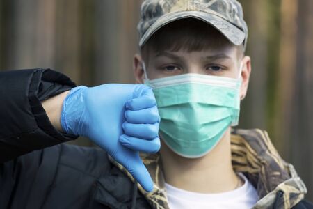 Boy in protective sterile medical mask on his face looking at camera outdoors. Air pollution, virus,  pandemic coronavirus concept.の写真素材